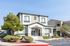 Charming apartment building with modern design, featuring a welcoming entrance and lush landscaping under a bright blue sky.