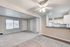 Inviting open-plan living area with a blend of carpet and sleek laminate flooring, bathed in natural light and adjacent to a modern kitchen featuring white cabinetry and stylish track lighting.