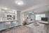 Modern open-concept living room with a stylish kitchen, featuring sleek bar stools, a cozy gray sofa, and large windows for ample natural light.
