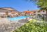 Inviting outdoor swimming pool area with sun loungers, orange umbrellas, and picnic tables, perfect for relaxation and leisure.