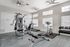 Modern fitness center with state-of-the-art equipment, including a treadmill, dumbbells, and multi-station gym machine, in a well-lit room with ceiling fans.