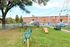 Charming apartment complex with a vibrant dog park featuring agility equipment, green spaces, and convenient seating under a sprawling tree.