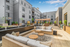 Modern apartment amenity deck featuring stylish outdoor seating, lush greenery, and a sleek water feature under a clear blue sky.