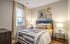 Cozy bedroom with a plush bed adorned with patterned cushions, chic art on the wall, and warm lighting from stylish table lamps.