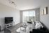 Bright and modern living room with sleek grey sofa, fluffy white rug, and large window with vertical blinds overlooking city view.
