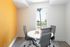 Bright and modern office space with a round table, sleek chairs, and a vibrant orange accent wall, overlooking a scenic outdoor view.
