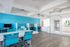 Modern office space featuring vibrant blue walls, sleek computer stations, and stylish seating, offering a bright and inviting work environment.