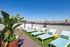 Stunning rooftop terrace with modern loungers, lush greenery, and panoramic city views under a clear blue sky.