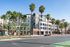 Modern luxury apartment complex with vibrant shops and palm-lined street under a clear blue sky, showcasing urban living at its finest.