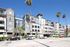 Contemporary urban apartment complex with stylish architecture, large balconies, and lush palm trees under a clear blue sky.