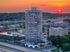 Breathtaking view of a modern high-rise apartment building at sunset, showcasing a vibrant cityscape with lush greenery and a striking skyline.