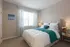 Model bedroom at our apartments in Marlborough, featuring carpeted flooring and a window with blinds and curtains.