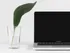 A computer next to a glass of water with a leaf in it. The computer's screen is black and the backdrop is white.