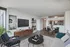Model living room at our apartments for rent in Flatiron, featuring wood grain floor paneling and a view of the kitchen.