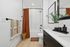 Bathroom with elevated finishes to include quartz counters, oversized mirror, soaking tub with subway tiles, and matte black finishes