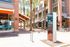 Vibrant urban scene with modern architecture, gleaming glass windows, and lush palm trees under a bright sky, featuring an inviting outdoor dining area perfect for entertainment.