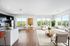 Bright and airy open-concept living and kitchen area with modern decor, elegant furnishings, and large windows offering stunning views of lush greenery.