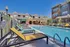 Charming apartment community with a sunlit swimming pool, surrounded by colorful lounge chairs and vibrant modern architecture.