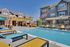 Inviting apartment community pool area with sun loungers, blue sky backdrop, and modern brick buildings.