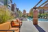 Inviting outdoor pool area with stylish orange seating and sleek sun loungers, nestled beside modern apartment buildings and lush foliage.
