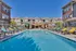Inviting outdoor pool area at modern apartment complex, featuring colorful lounge chairs and landscaped surroundings under a bright blue sky.