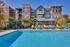 Charming apartment building with a vibrant outdoor pool area, colorful lounge chairs, and lush green landscaping perfect for relaxation and social gatherings.