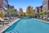 Inviting outdoor pool area with modern lounge chairs, surrounded by lush greenery and contemporary brick apartment buildings basking in sunlight.