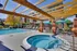 Inviting outdoor pool area with sun loungers, a hot tub, and stylish pergola, surrounded by vibrant landscaping and modern apartments.