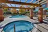 Chic apartment complex featuring a sunlit outdoor pool area with relaxing lounge chairs and a cozy hot tub under a stylish pergola.