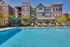 Modern apartment complex with a vibrant pool area, featuring colorful lounge chairs and shaded seating, perfect for relaxation and leisure.