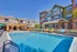 Charming apartment complex with vibrant poolside seating, modern architecture, and a spacious swimming pool under clear blue skies.