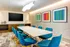 Modern meeting room with vibrant blue chairs, a sleek white table, and colorful abstract art on the walls.