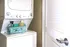 Compact laundry area with modern stacked washer and dryer, featuring a neatly organized storage basket with cleaning supplies beside a stylish louvered door.