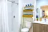 Elegant bathroom featuring a sleek white shower, modern vanity with a chic plant, and a stylish storage ladder with woven baskets.