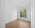 Bright and airy room with large window, elegant wooden flooring, and fresh white walls, offering a serene view of lush trees.