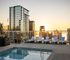 Luxurious rooftop pool with sun loungers and breathtaking skyline views at sunset, perfect for relaxation.