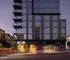 Elegant modern apartment building with glowing entrance, labeled Ancora, showcasing sleek architecture and ample parking.