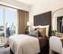 Chic and cozy bedroom featuring a plush bed with decorative pillows, elegant desk with mirror, and a stunning city view through large windows.