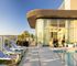 Luxurious rooftop pool area with sleek lounge chairs, panoramic city views, and modern glass-encased lounge in a vibrant high-rise setting.