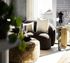 Elegant living room with a modern curved sofa, plush pillows, and a stylish ottoman in front of a bright window, featuring chic decor and contemporary art.
