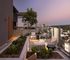 Chic rooftop terrace with cozy seating, lush planters, and stunning city skyline views at dusk.