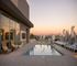 Luxurious rooftop pool deck at sunset with stunning city skyline views, stylish loungers, and elegant seating.