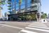 Modern urban apartment building with sleek glass facade and balconies, situated on a vibrant city street