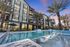 Luxury apartment complex with modern architecture and palm-lined swimming pool, set against a vibrant sunset sky.