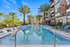 Luxurious apartment complex with a crystal-clear swimming pool surrounded by palm trees and sleek lounges, offering a tropical resort-style ambiance.