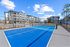 Modern apartment complex with a vibrant blue tennis court under a clear blue sky, offering recreational amenities.