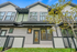 Charming townhome exterior with modern windows and sleek black trim framed by vibrant greenery and a clear blue sky.