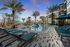 Luxurious apartment complex pool area with stylish lounge chairs, tropical palm trees, and vibrant sunset backdrop.