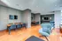 Modern communal space with sleek wooden flooring, comfortable seating, and elegant dining area. Features contemporary decor and wall-mounted TVs, ideal for social gatherings.