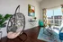 Chic and vibrant living room with a hanging wicker chair, abstract art, colorful curtains, and a sunny balcony view.